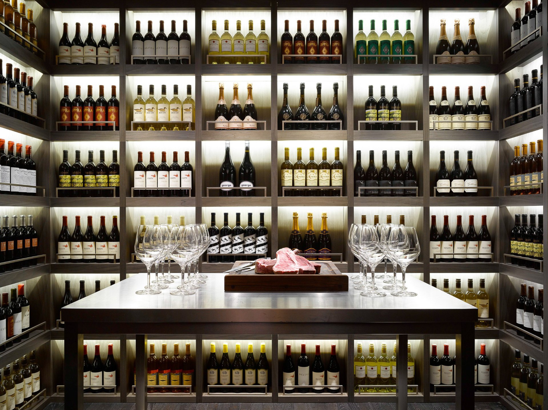 The wine room of The Emblem Prague, glasses on the table before walls of lit bottles