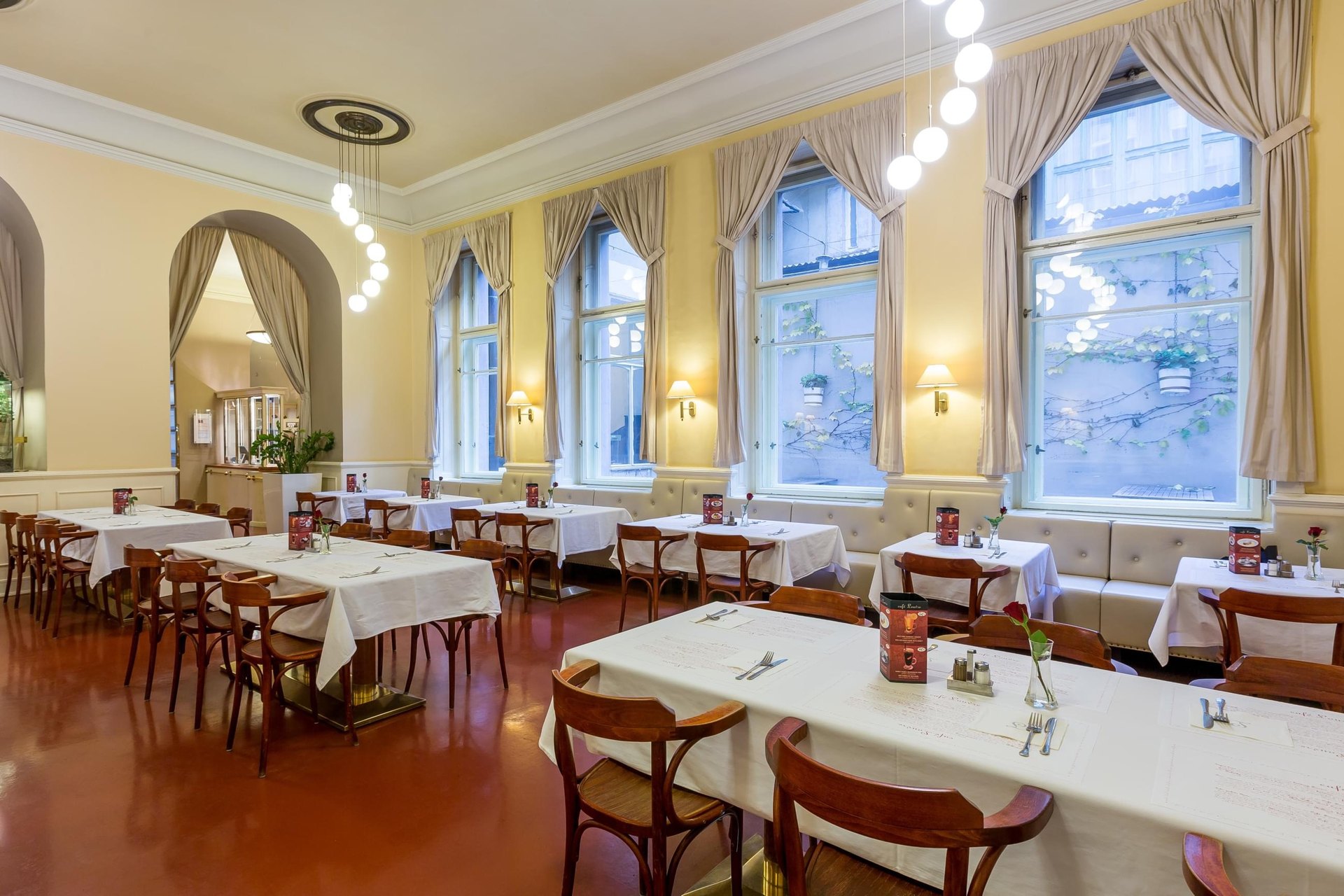 A cream dining room of Café Louvre, tables laid in white beneath tall curtained windows