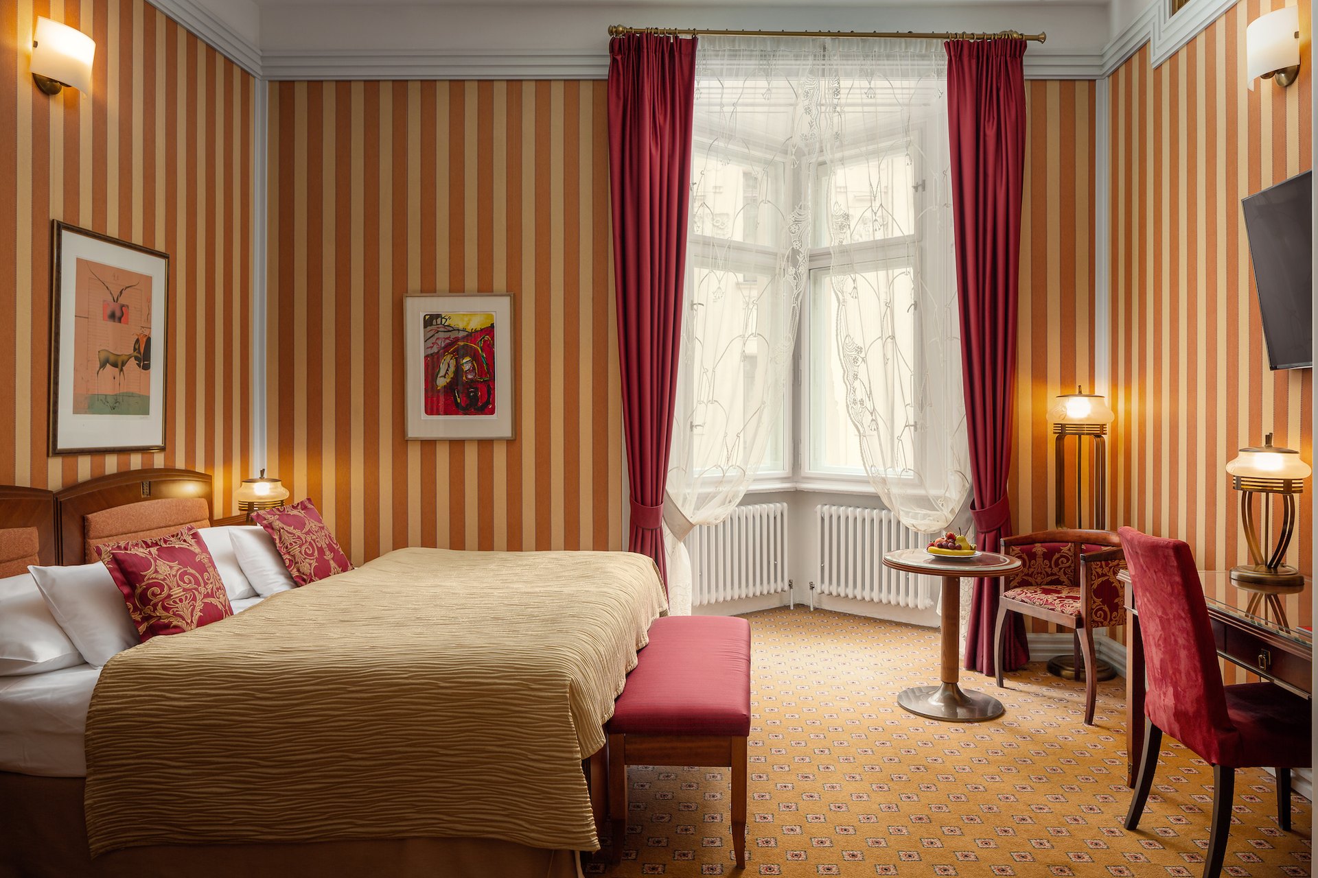 A room at the Hotel Paris with striped walls, red velvet chairs and a bay window
