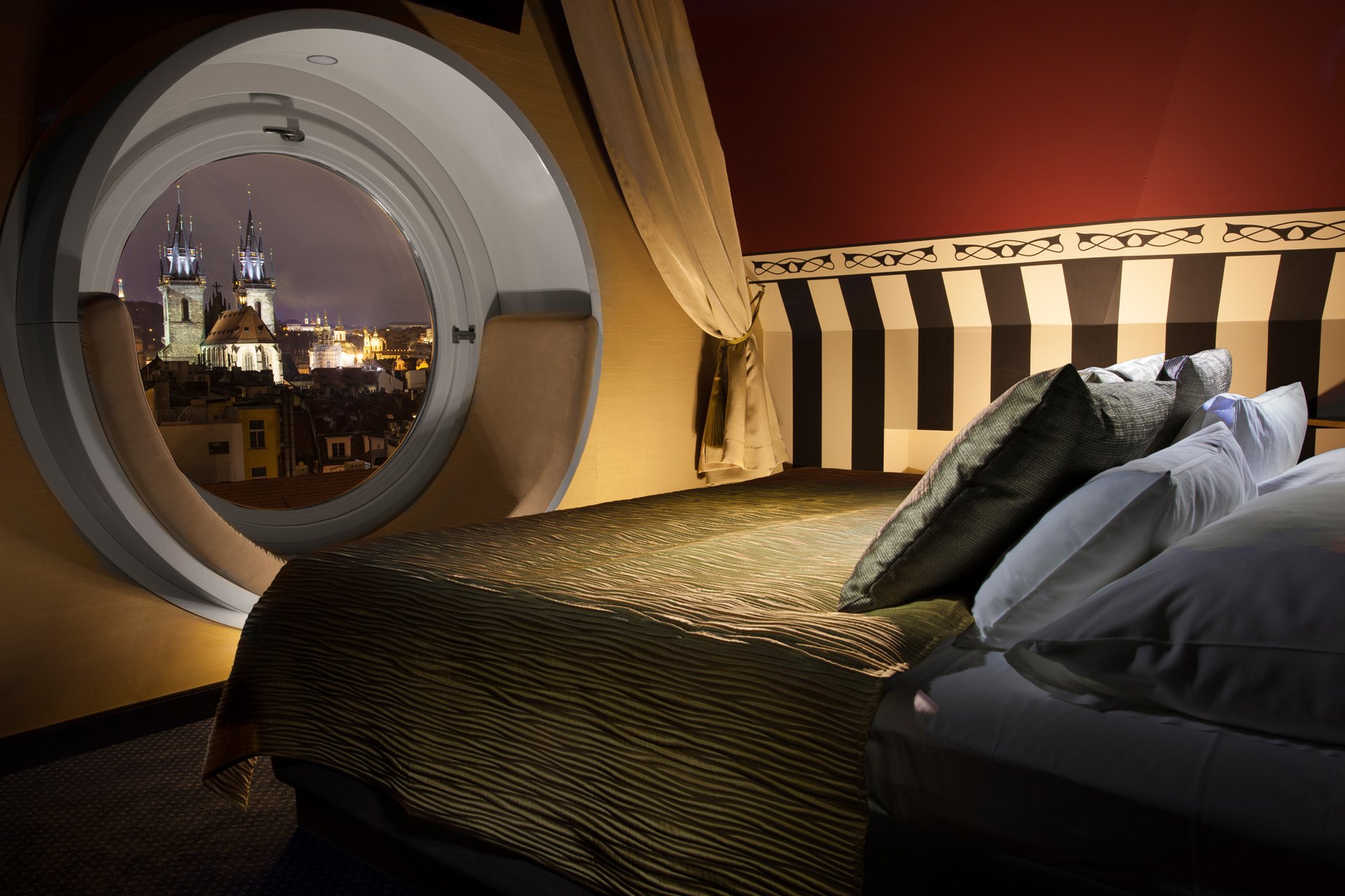 The Tower Suite of the Hotel Paris, its round window framing the spires of the Týn church at night