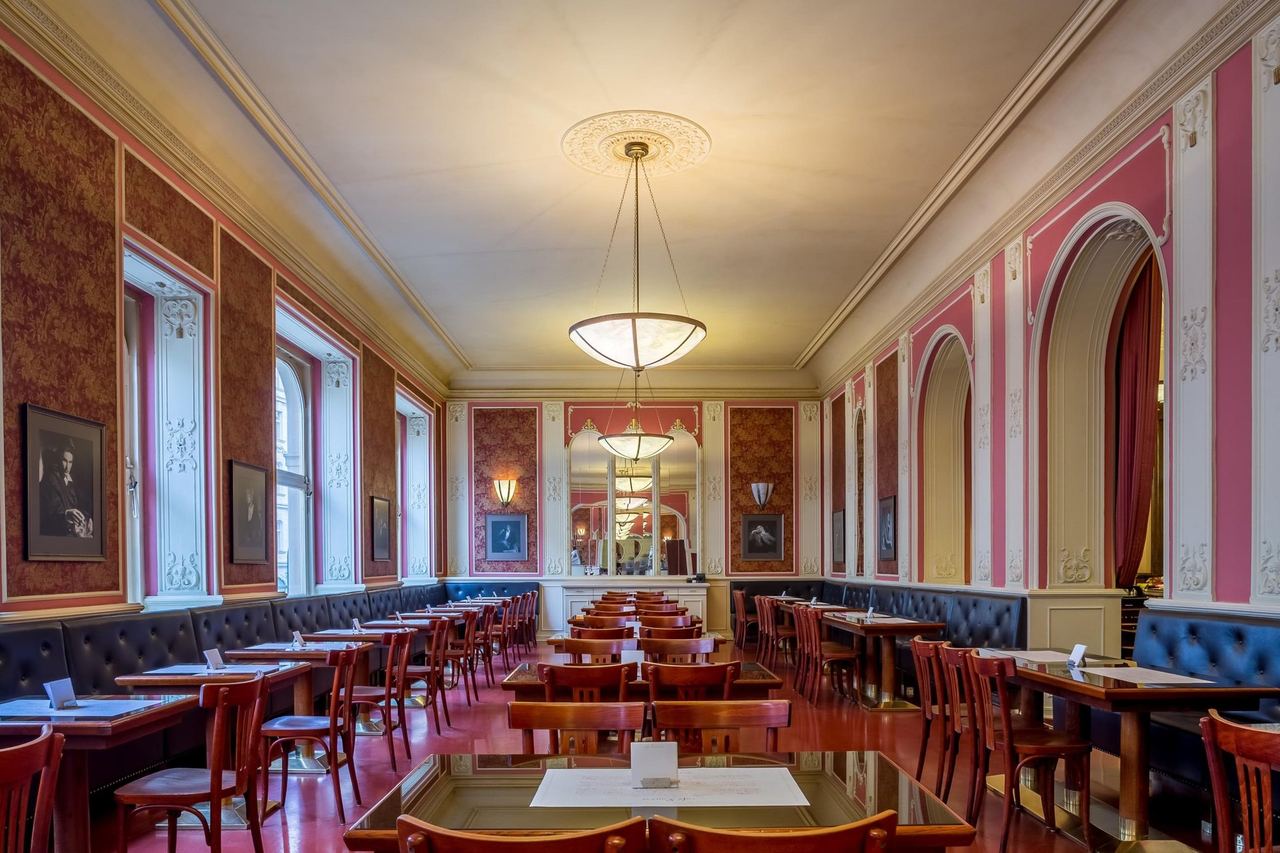 The pink salon of Café Louvre, with its long banquettes, arched windows and glass pendant lamp